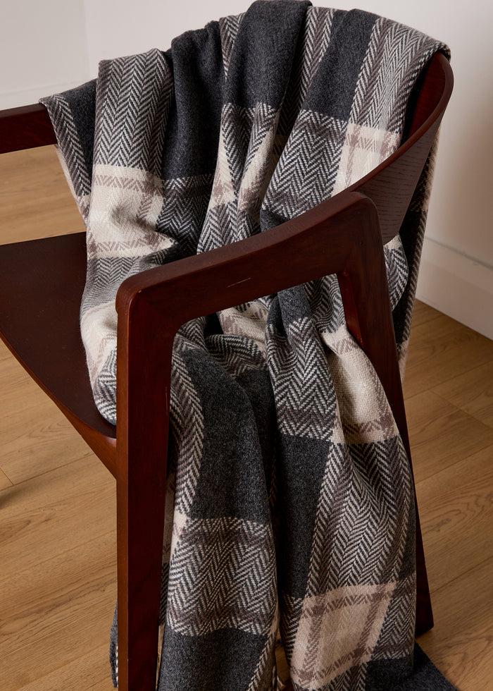 draped over a chair  the Foxford Dun Chaoin Lambswool and Cashmere Throw blends luxury and comfort. With its plush lambswool and cashmere fabric, this throw provides warmth while still exuding elegance. The timeless grey and mink Oxford check design