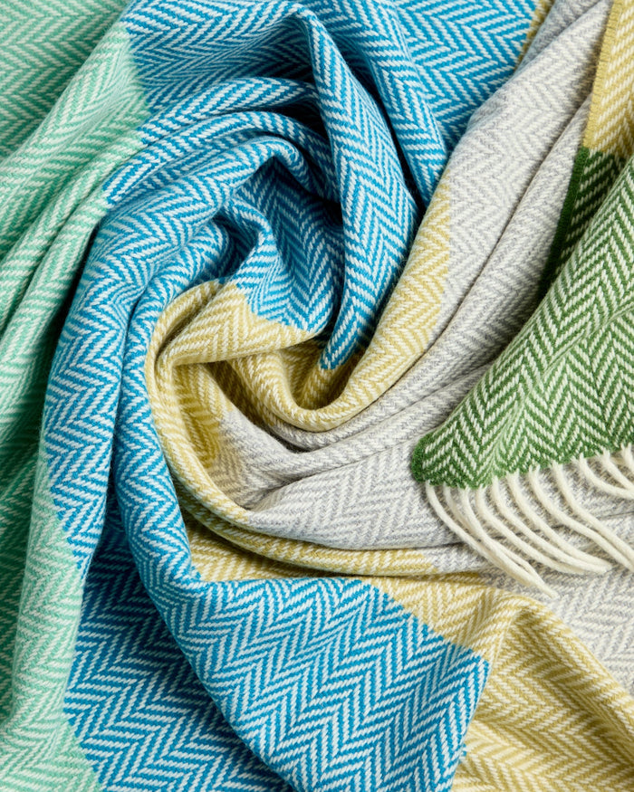 Luxurious Foxford Garavogue Cashmere and Lambswool Throw Featuring a vibrant herringbone pattern in blues, greens, and yellows, with soft fringed edges. Woven in Foxford’s historic mill in County Mayo, Ireland.