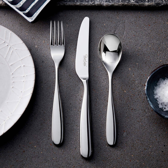 Stainless steel cutlery set on a dark surface with a plate and small bowl.